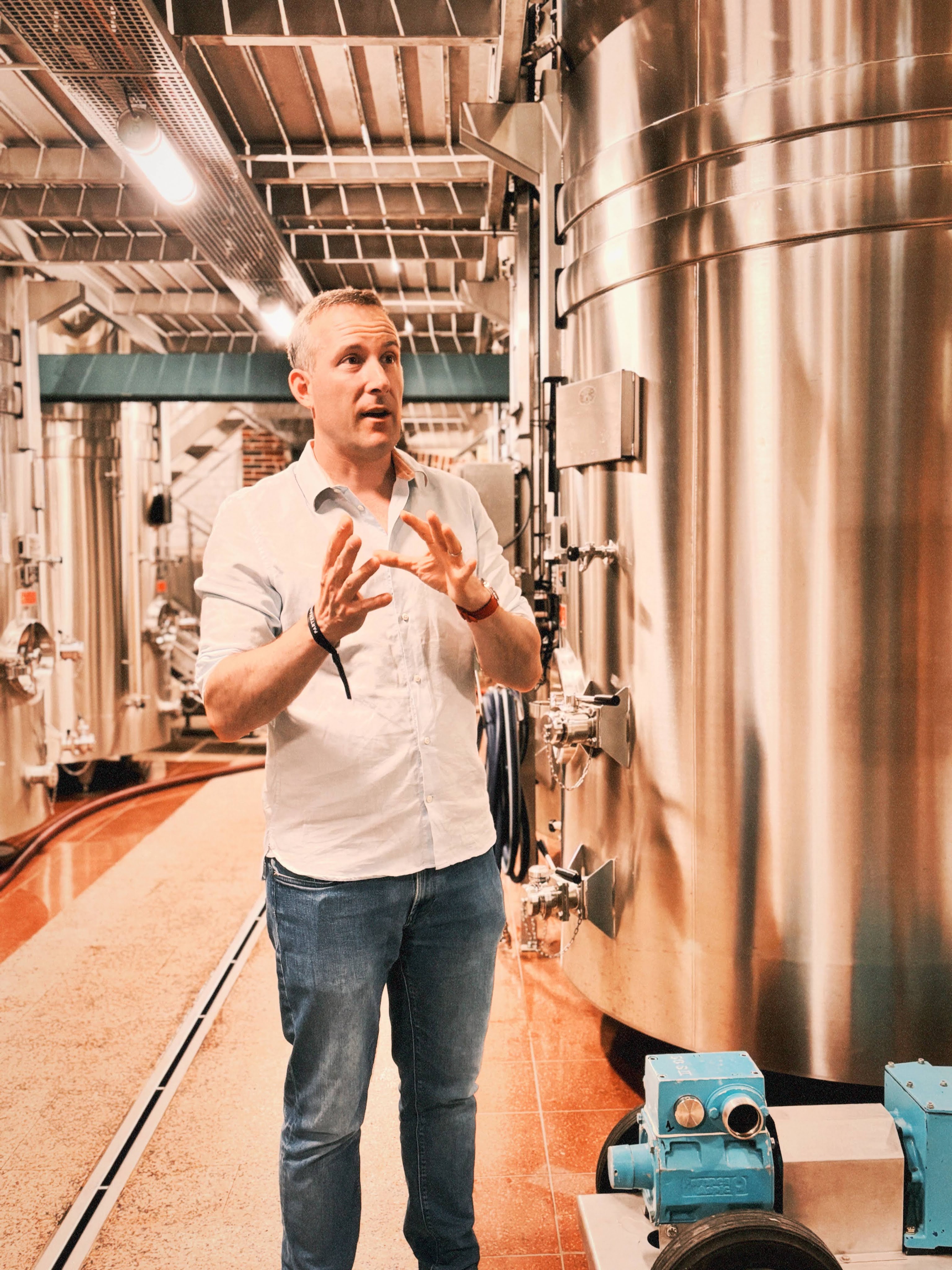 A man explaining a process in a facility surrounded by large metallic tanks and equipment.
