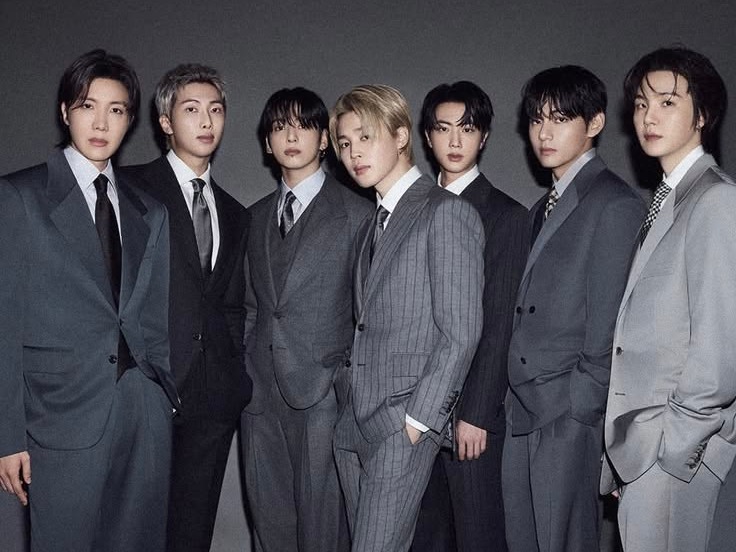 A group of seven men dressed in stylish suits poses confidently against a dark background, showcasing a mix of formal attire and modern fashion.