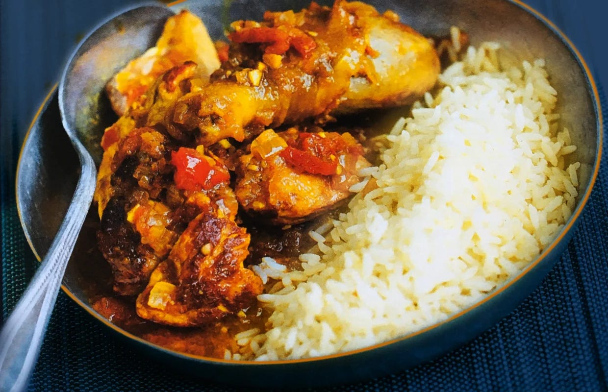 A plate of chicken in spicy sauce served with white rice, garnished with chopped tomatoes.