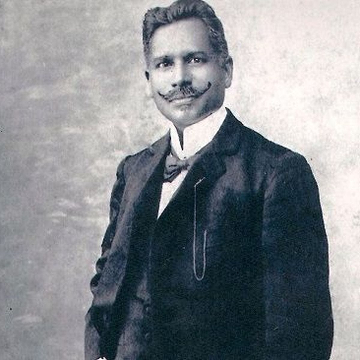 A black and white portrait of a man with a prominent mustache, wearing a formal suit and bow tie, posing confidently.