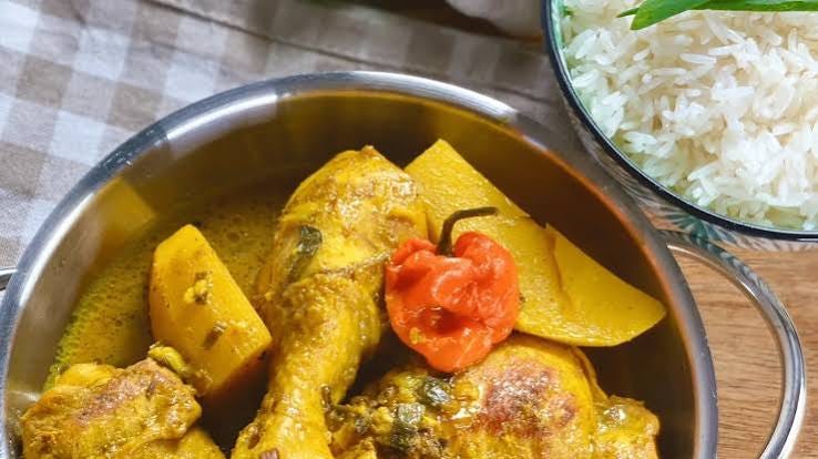 A serving of chicken stew with yellow curry, pumpkin, and a pepper, accompanied by a side of white rice.