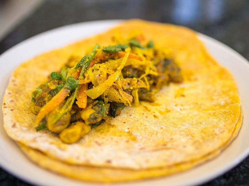 A close-up of a flatbread topped with a colorful vegetable stir-fry, including carrots, green beans, and spices.